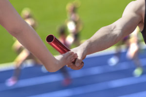 29300720 - male relay runner hands over the red baton to female runner